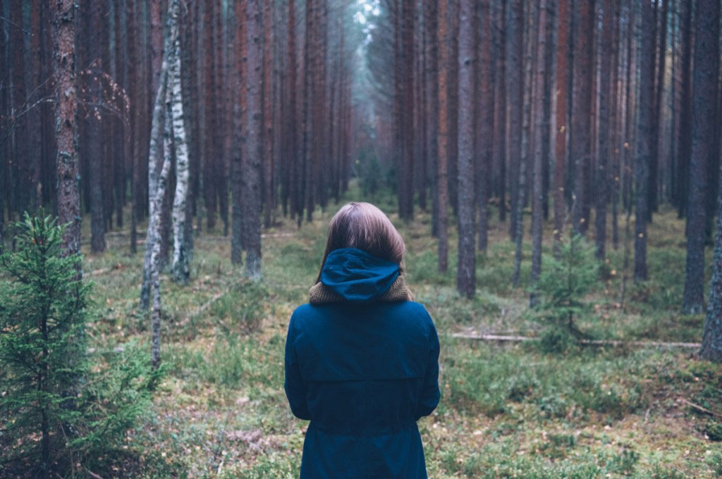 Woman stands at the entrance to a forest on a cool day wearing a blue coat