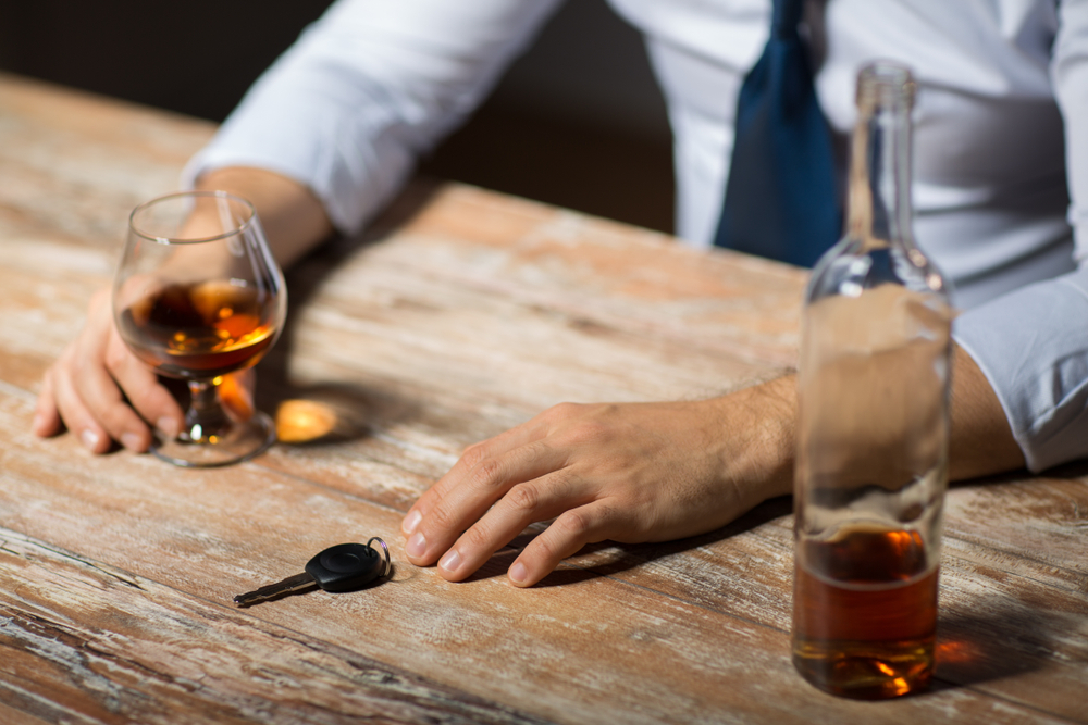 a person sitting at a bar with a drink in one hand and his car keys sitting just out of reach of the other. 