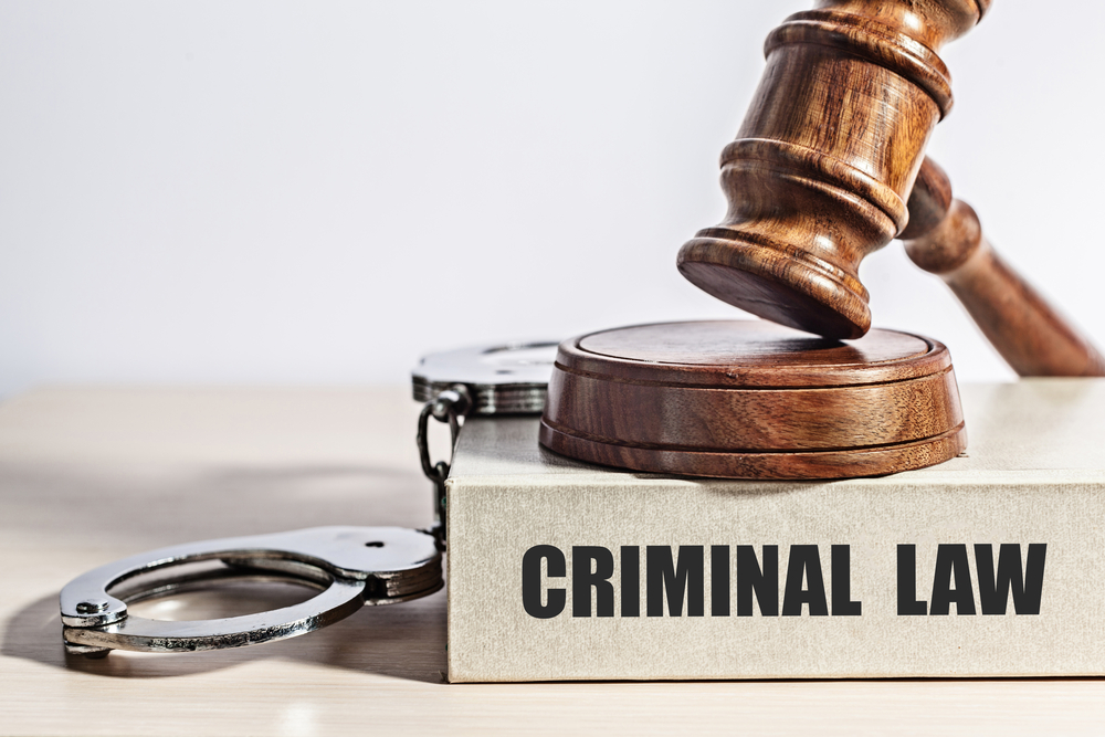 a pair of handcuffs and a judges gavel sit atop a book entitled Criminal Law.